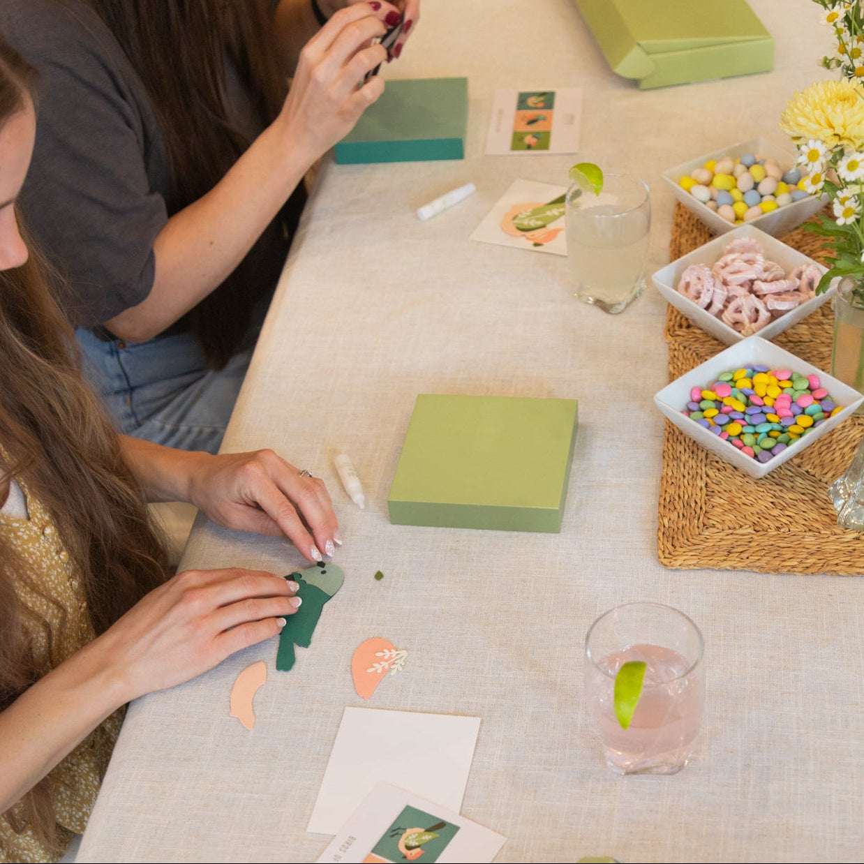 Two women at a table with craft supplies and snacks, engaged in a craft activity.