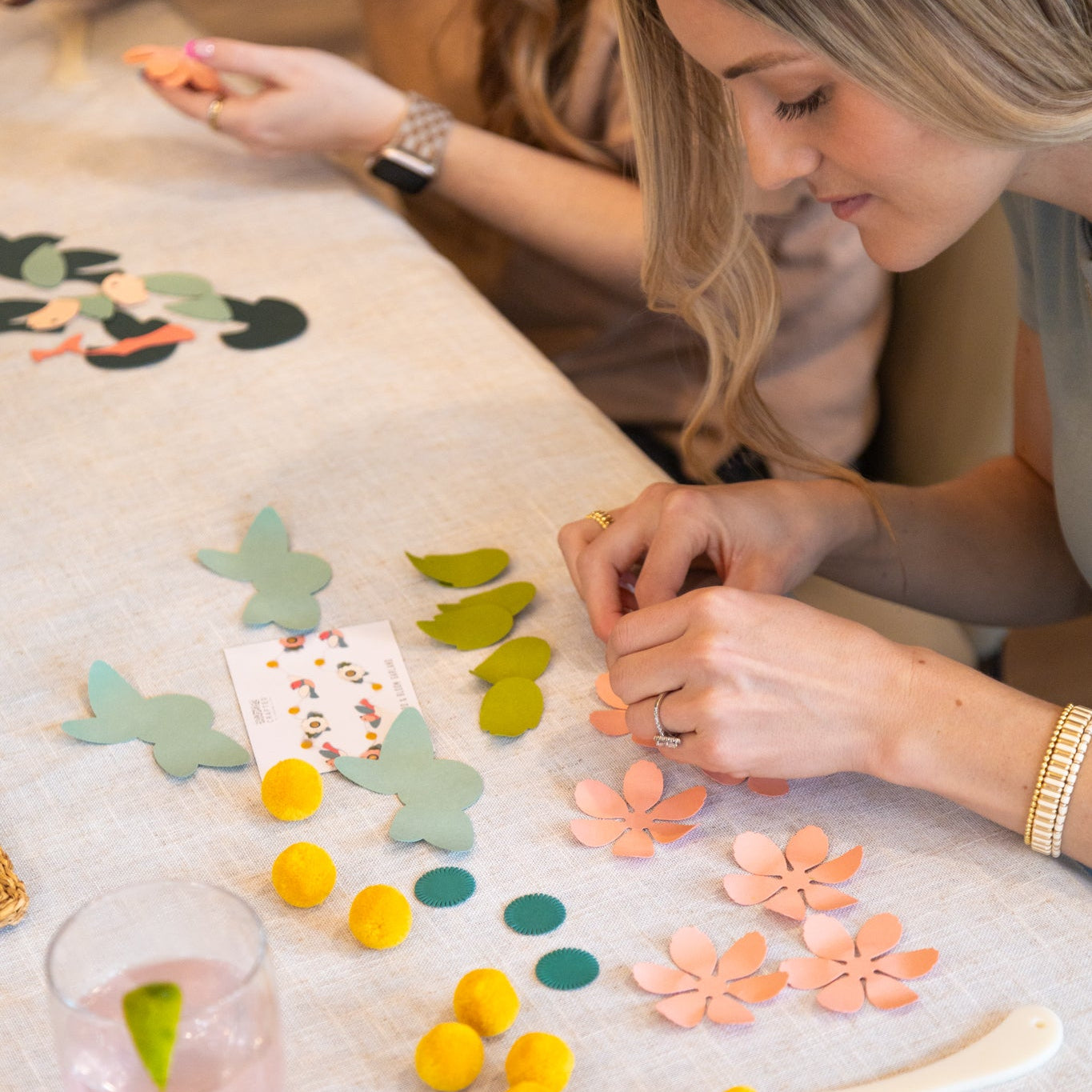 Two women working on a craft project with colorful paper flowers and leaves on a table.