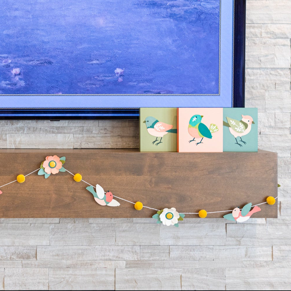Decorative mantel with a garland, small paintings, and a TV displaying water lilies.