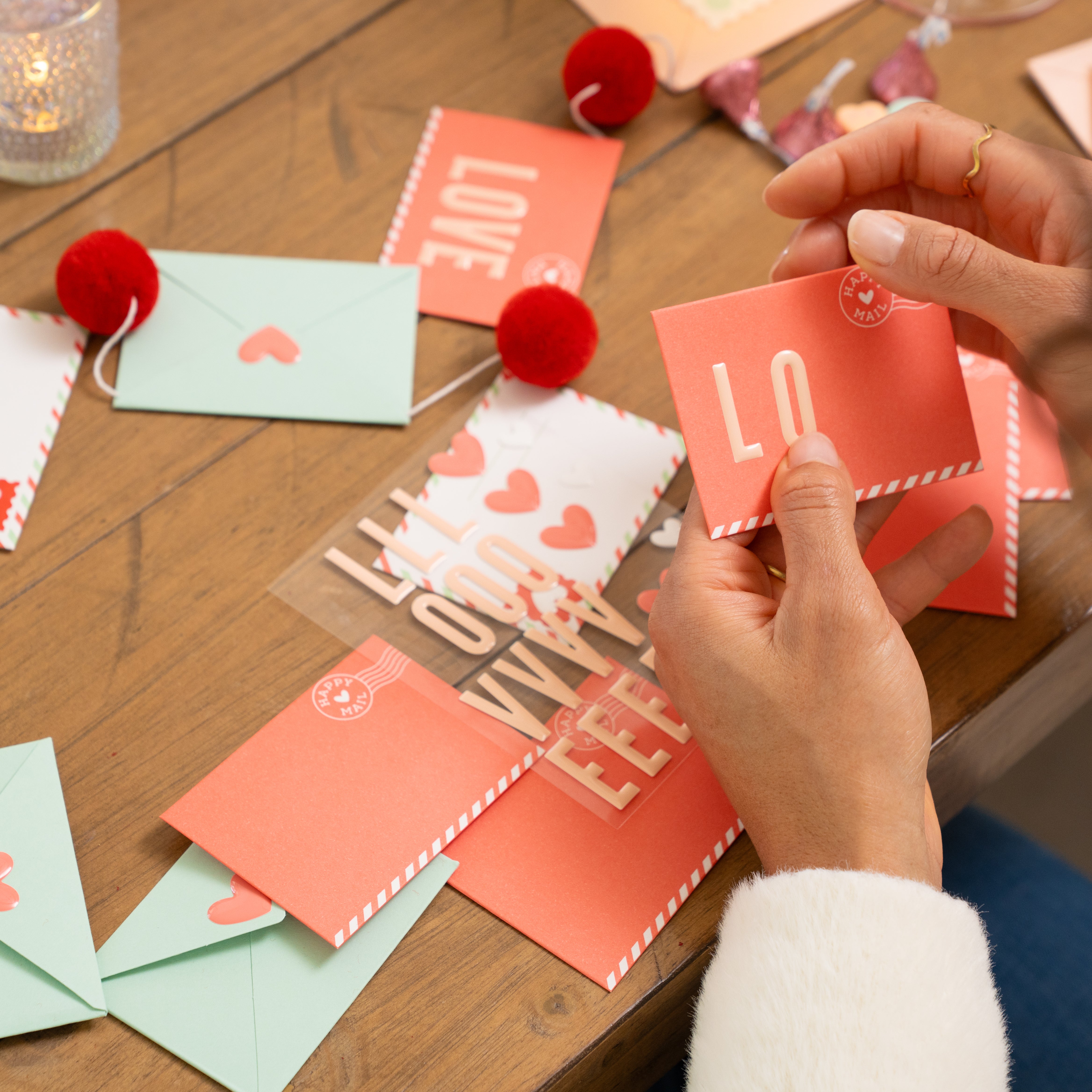 Person arranging small Valentine's love notes onto a garland on a wooden table