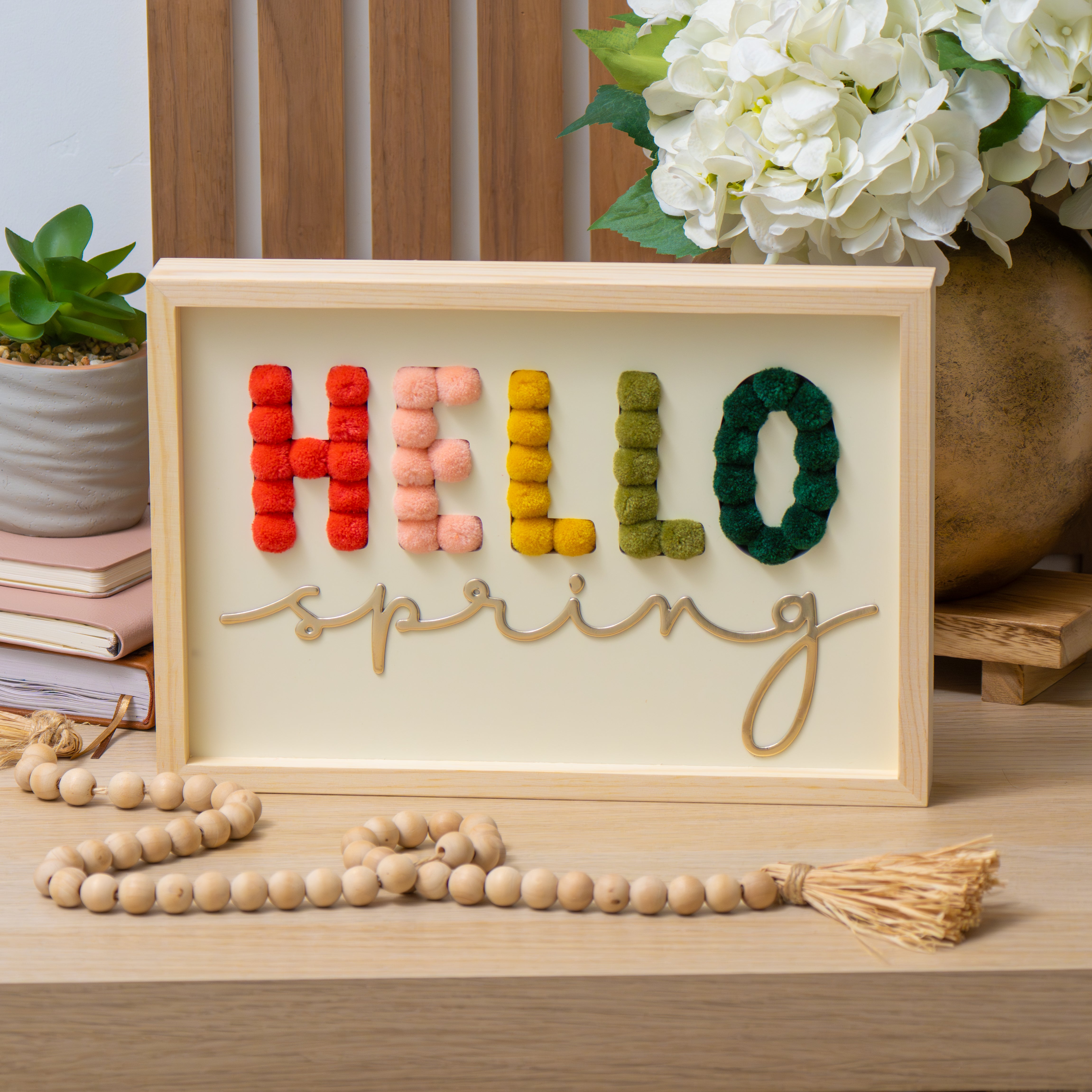 hello spring sign crafted from pompoms displayed on a table with flowers and books