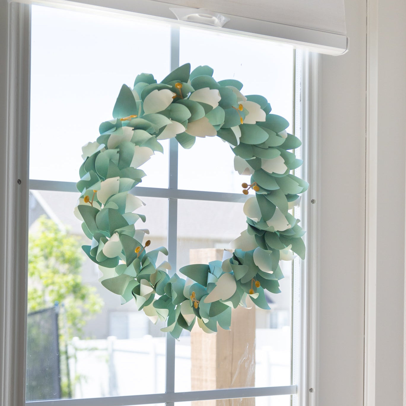Decorative paper wreath with green leaves and white flowers on a glass door.