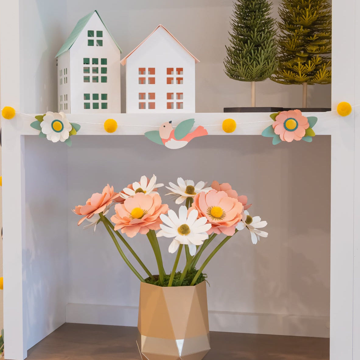 Decorative shelf with small houses, trees, and a vase of flowers.