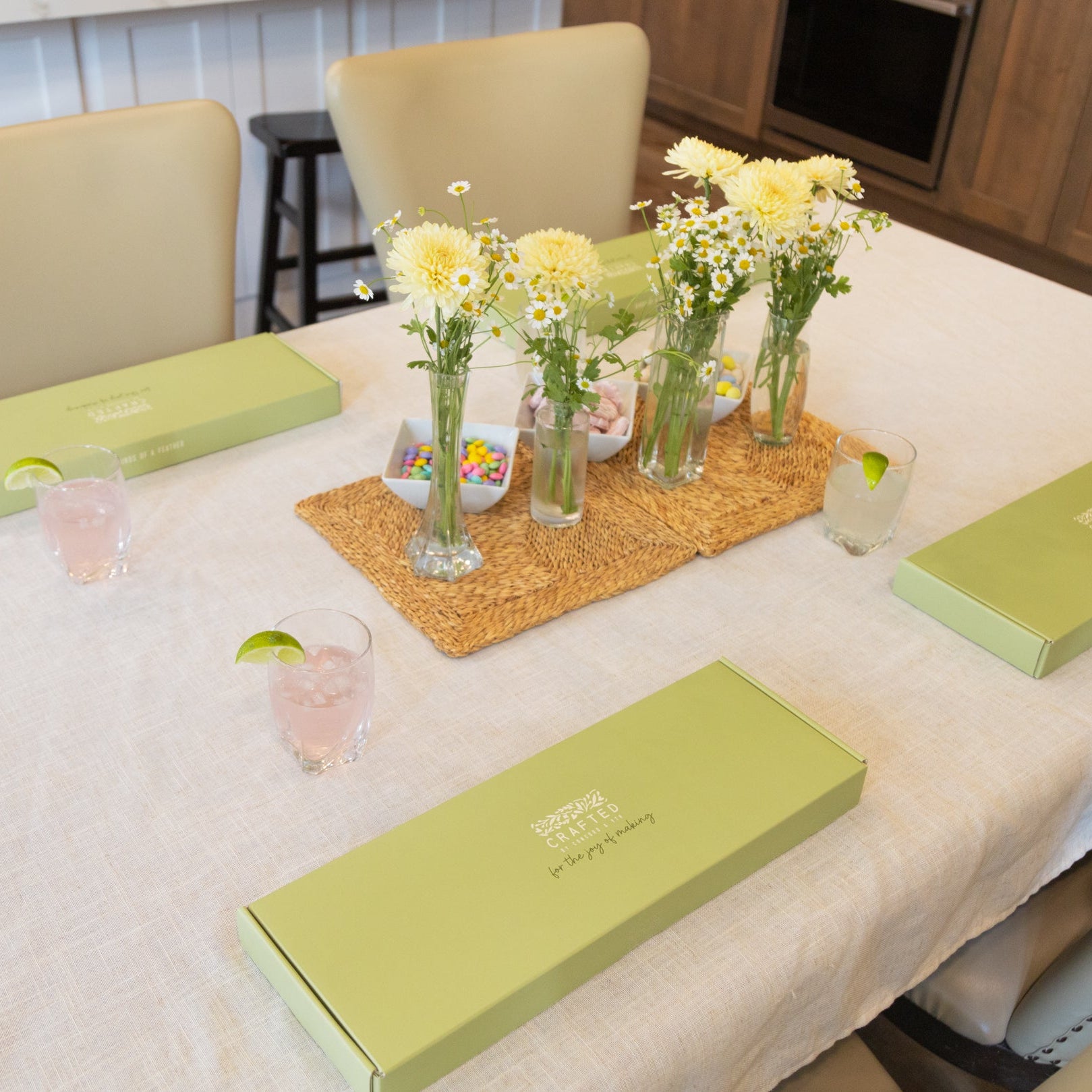 Dining table with DIY craft kit boxes, flowers, and drinks in a casual setting.