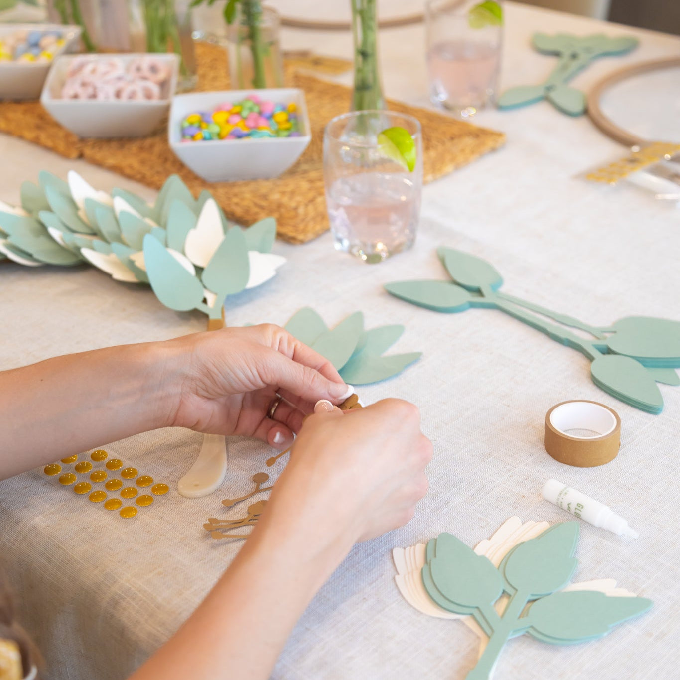 Person crafting with paper leaves on a table with flowers and decorative items.