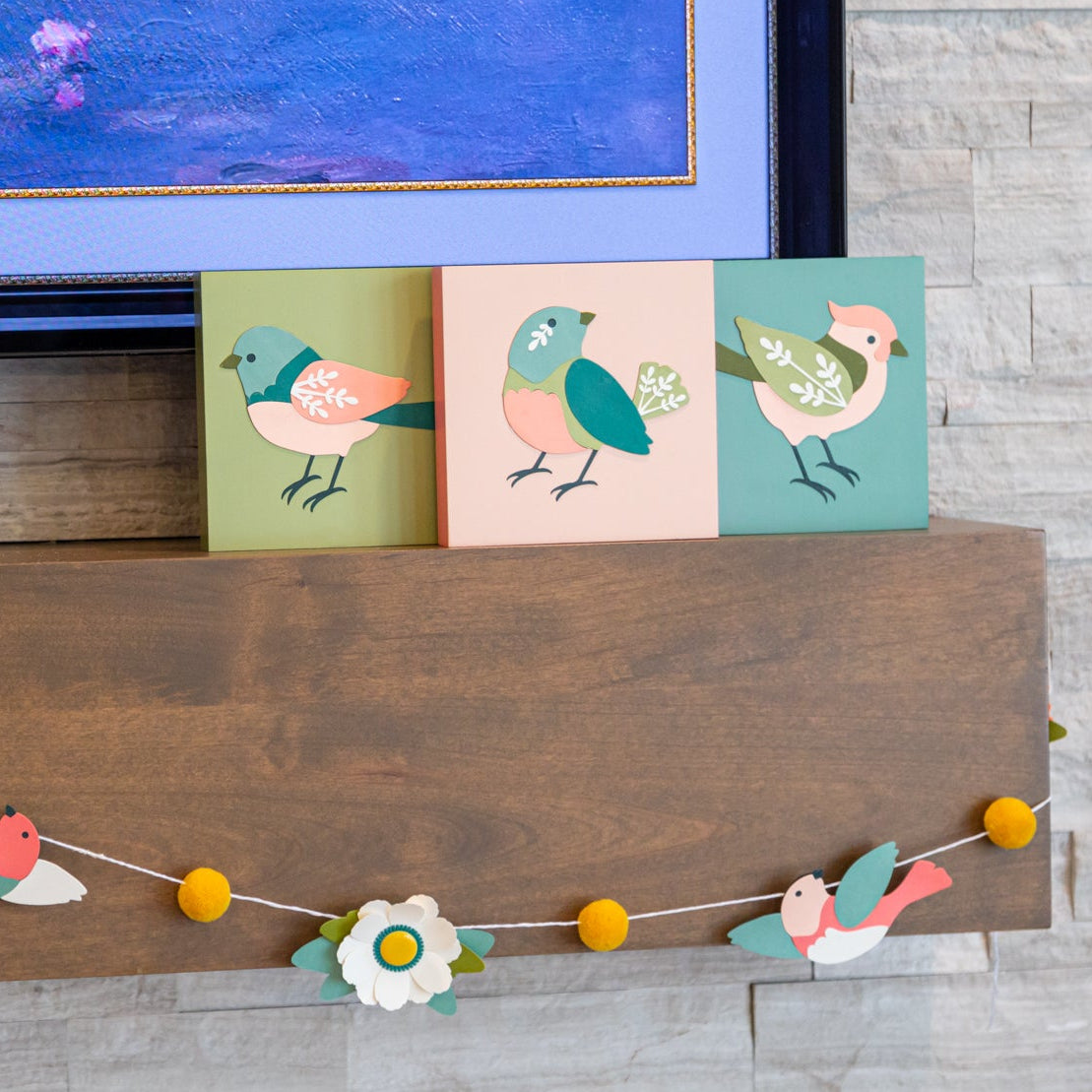 Decorative craft garland with bird blocks and flower designs on a fireplace mantle.