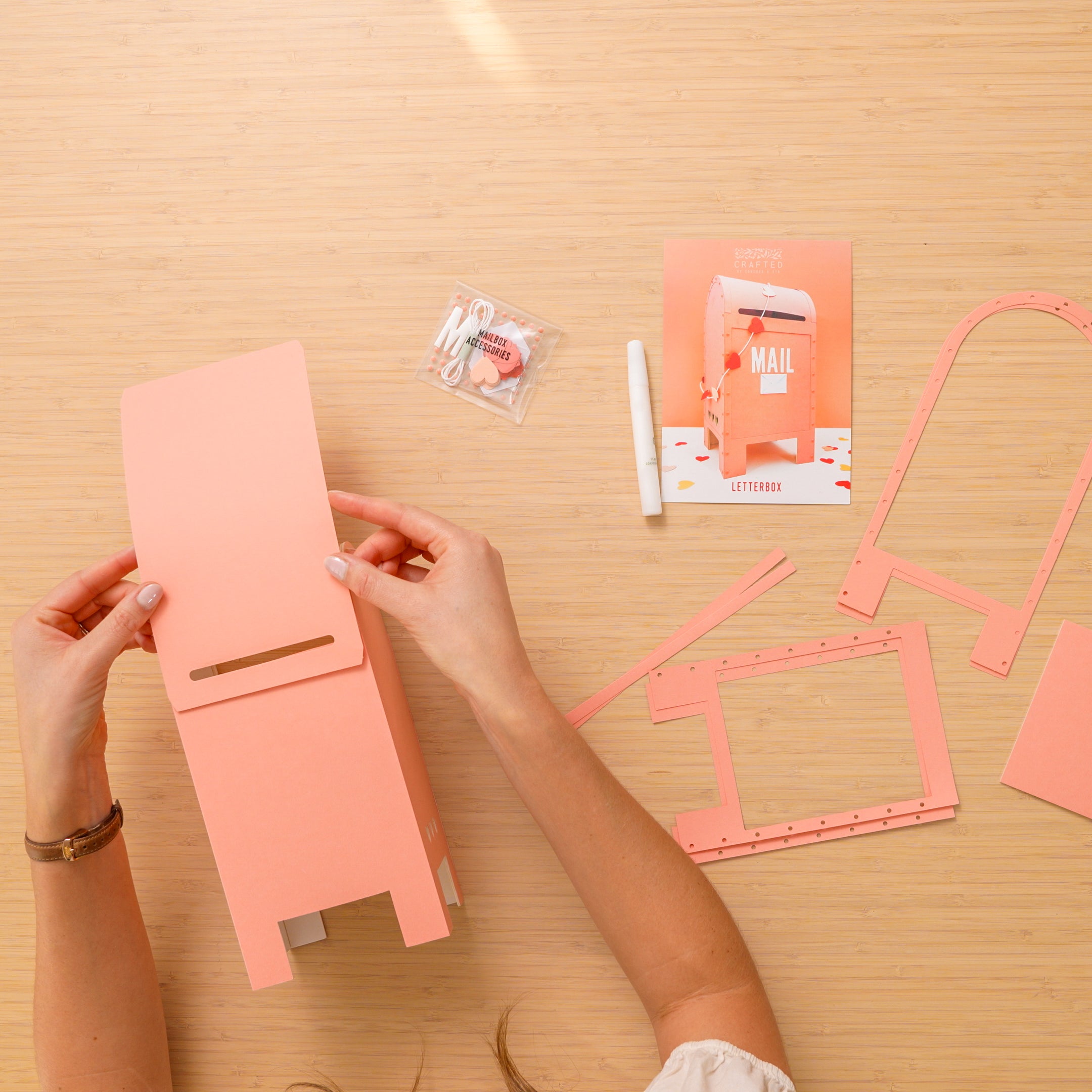 Person assembling a pink craft kit mail box on a wooden table