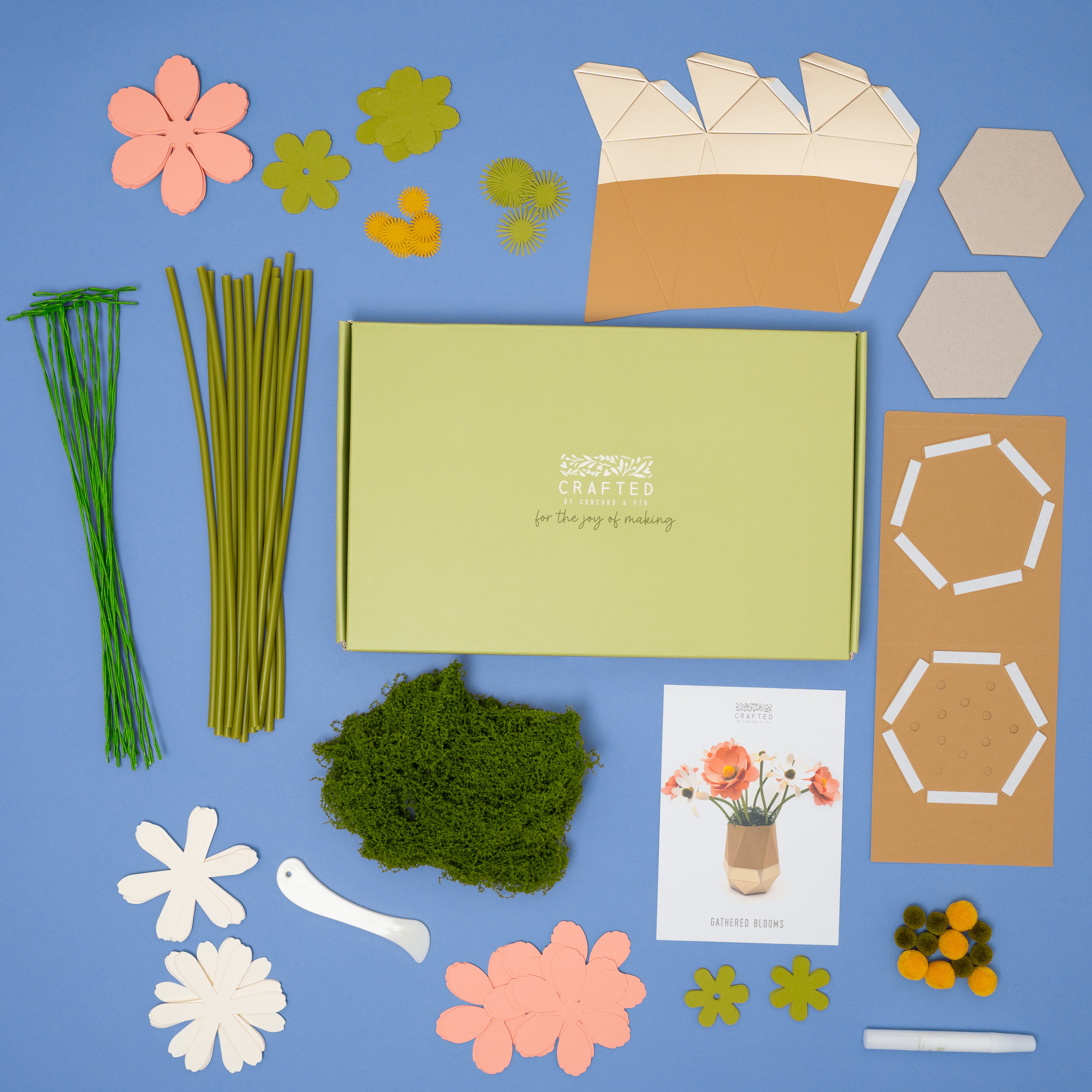 Crafting kit with paper flowers, floral wire stems, moss, and decorative elements on a blue backgrounsd